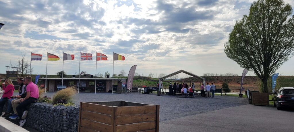 Clay shooting venue with flags from multiple countries, Beretta sponsor banners, and participants gathering under a tent during an international event.